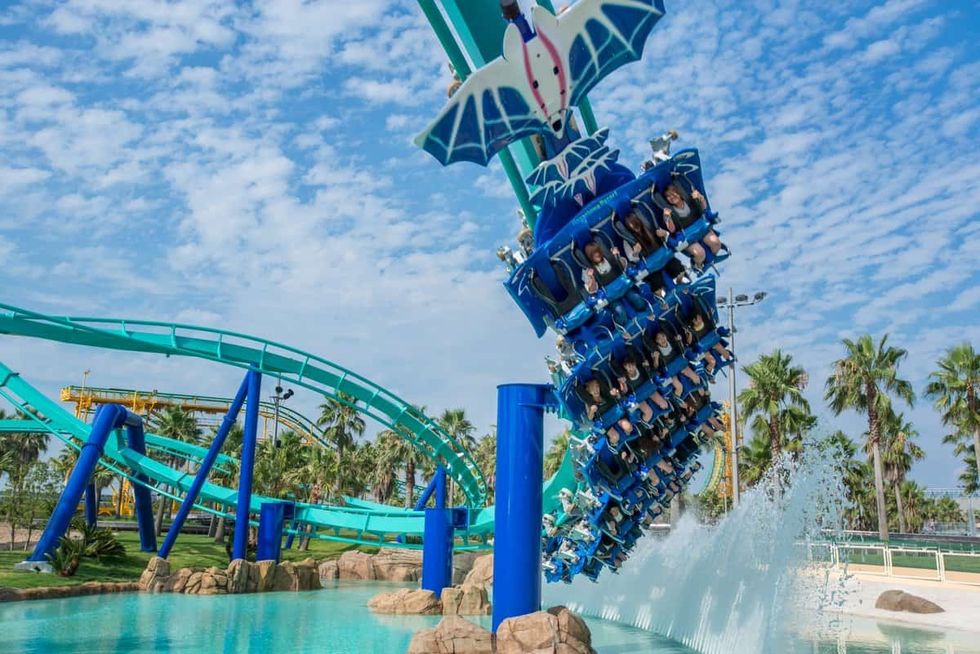 Roller coaster riders inverted above a splash pool on a sunny day.
