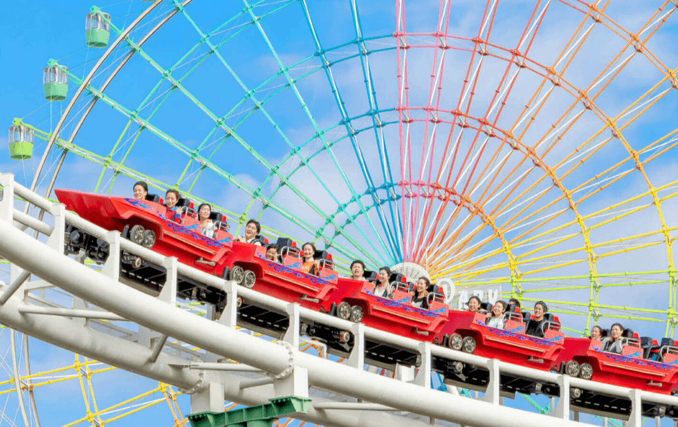 Roller coaster riders scream with joy, rainbow Ferris wheel in background.