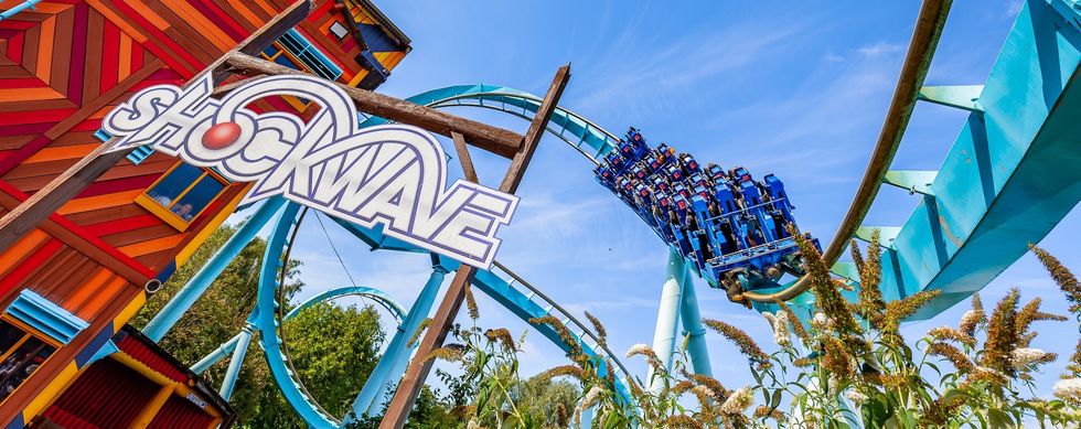 Roller coaster "Shockwave" with riders on a blue track against a clear blue sky.