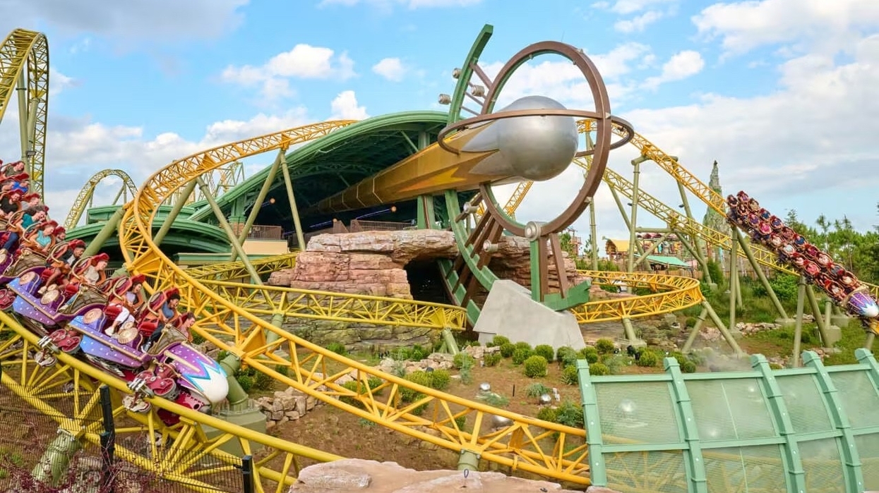 Roller coaster with a looping track and riders, set against a blue sky with clouds.