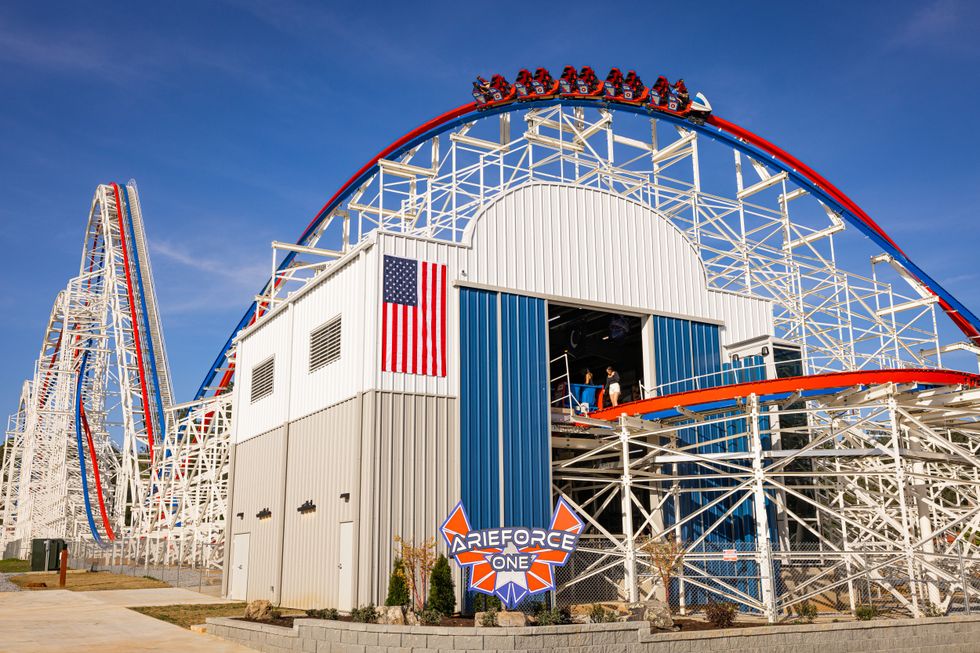 Roller coaster with an American flag, train on top, and blue sky background.