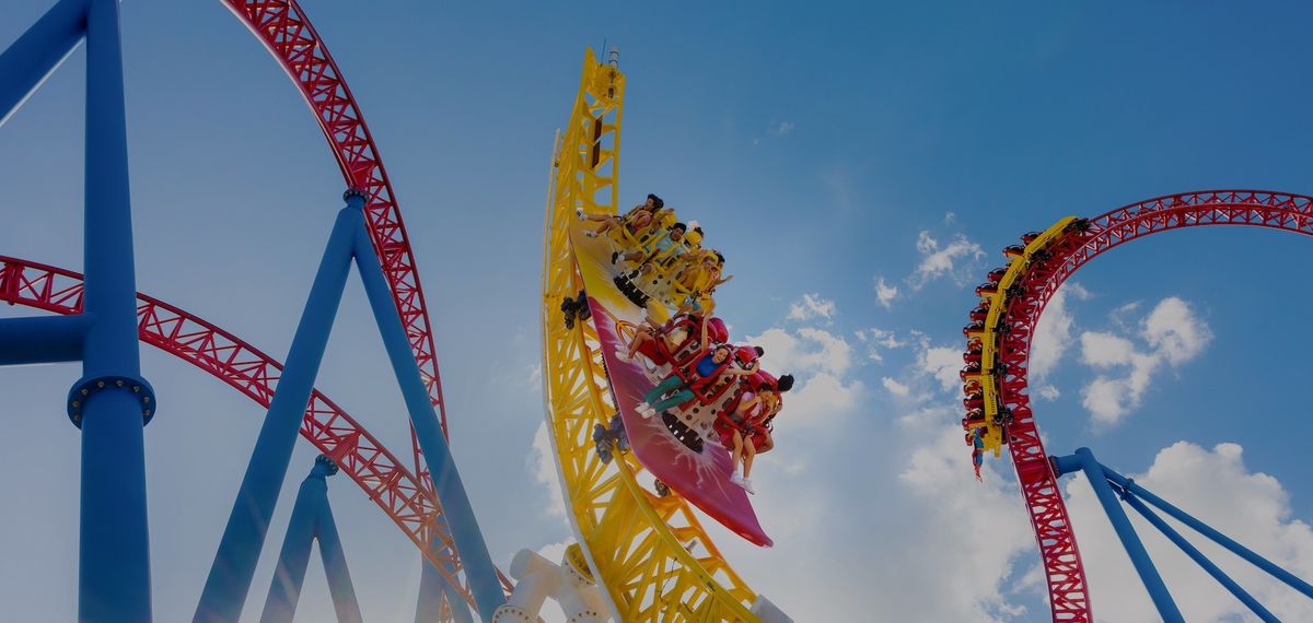 Roller coaster with colorful rails and riders against a clear blue sky.