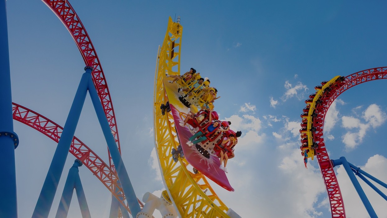 Roller coaster with colorful rails and riders against a clear blue sky.