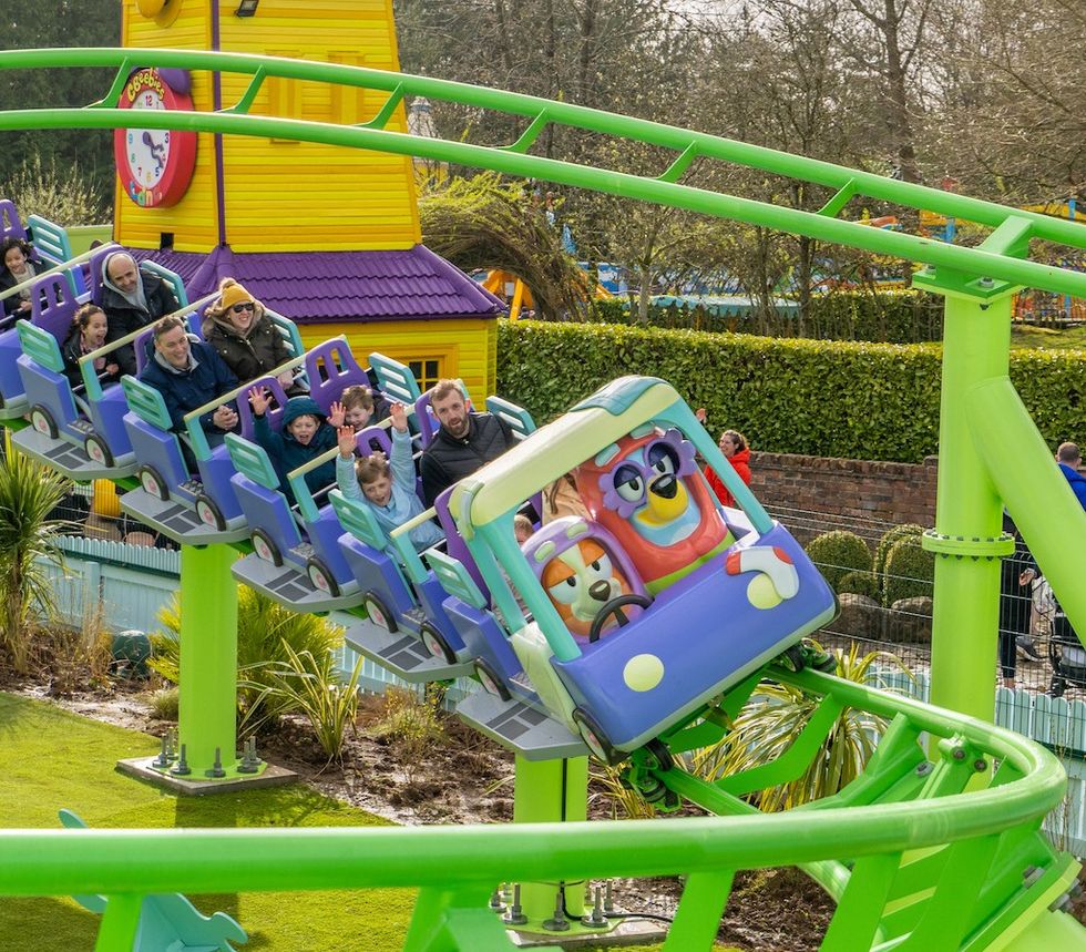 Roller coaster with families, cartoon cars, and colorful track at an amusement park.