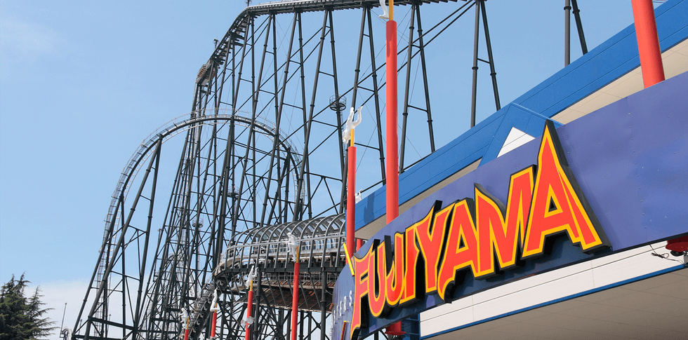 Roller coaster with "FUJIYAMA" sign in the foreground, under a clear blue sky.