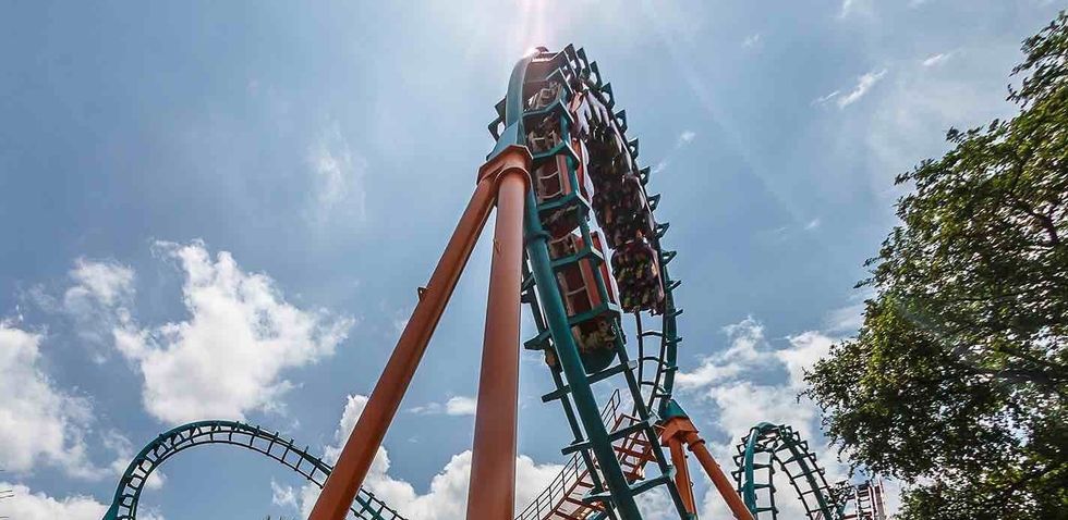Roller coaster with loops against a sunny blue sky, surrounded by trees.