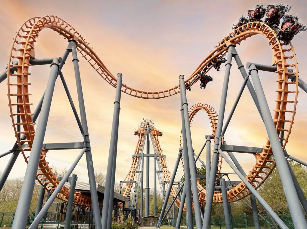 Roller coaster with loops and riders against a sunset sky at Parc Bagatelle
