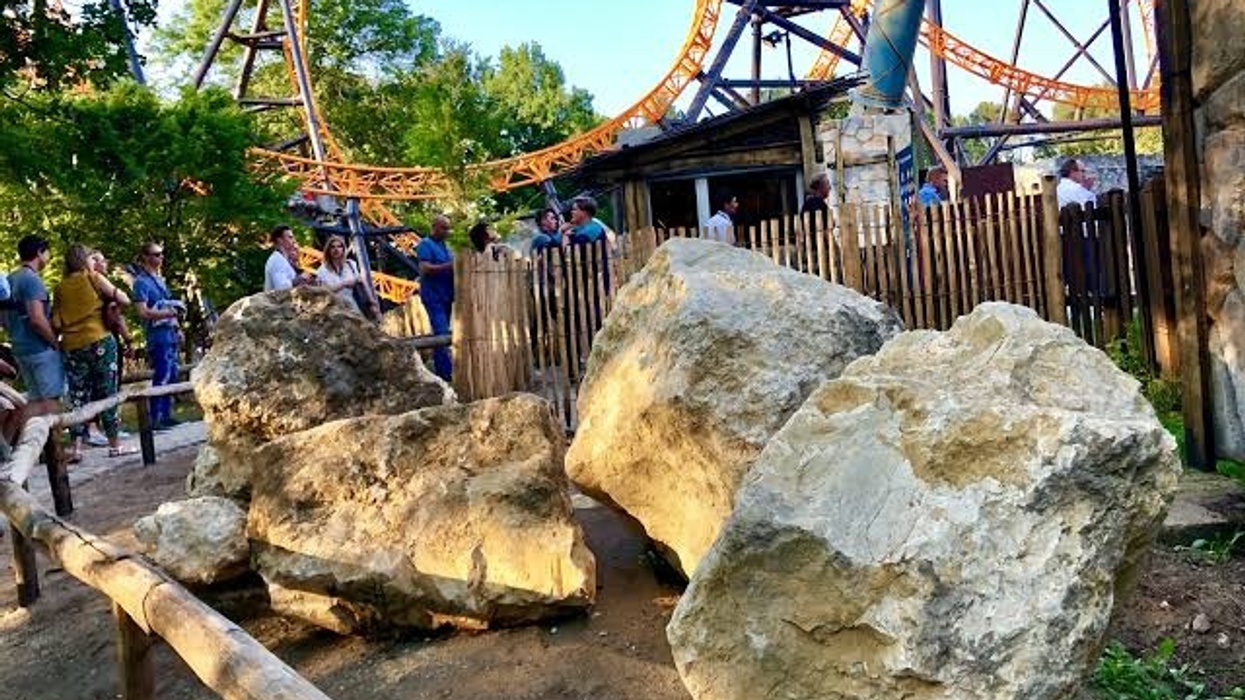 Roller coaster with people waiting in line, large rocks in the foreground.
