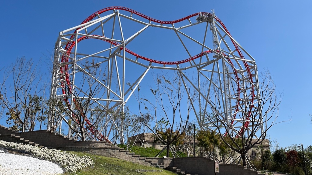 Roller coaster with red and white tracks, Zamperla Double Heart, against a clear blue sky and trees below.