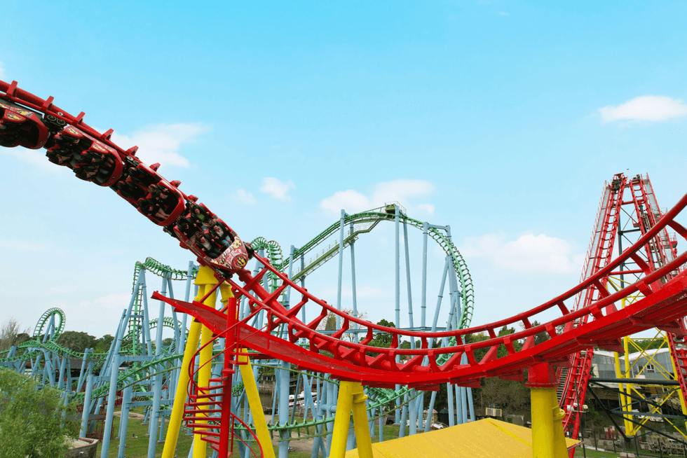 Roller coaster with red track and loops under a bright blue sky at Parque de la Costa