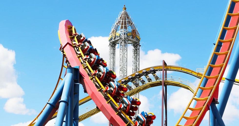 Roller coaster with riders twists at an amusement park under a clear blue sky.