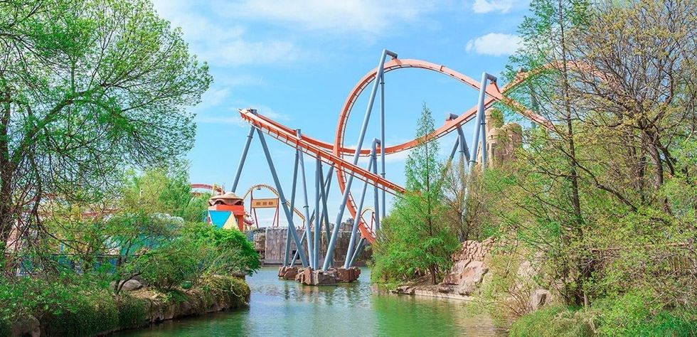 Roller coaster with twisting tracks surrounded by trees and water at happy valley beijing