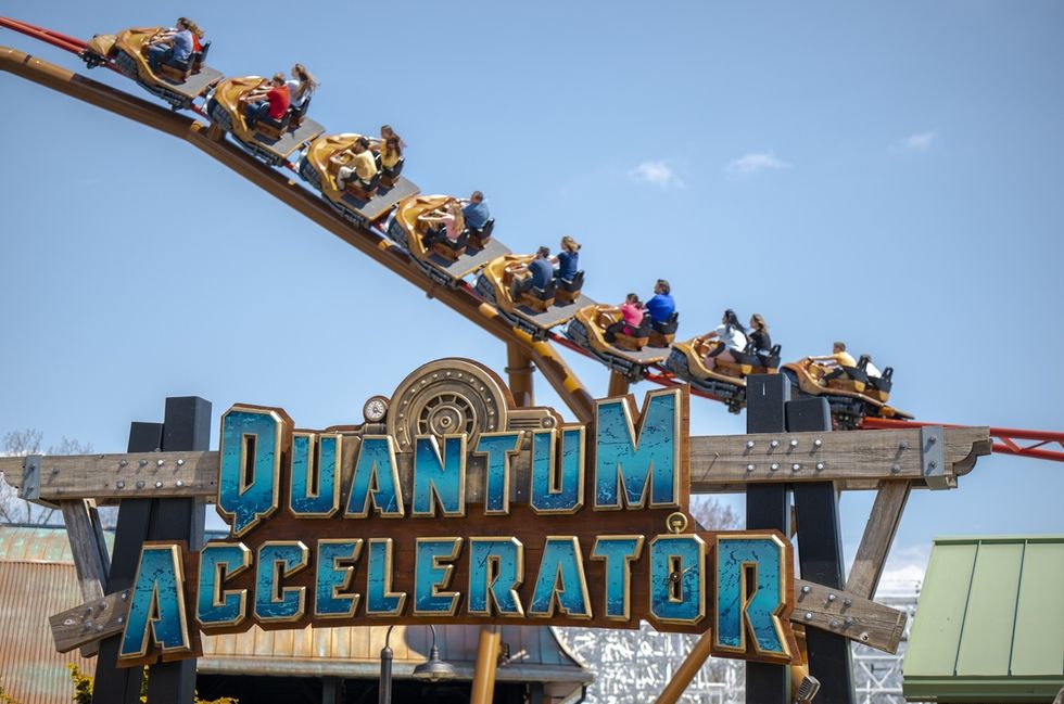 Rollercoaster "Quantum Accelerator" with riders on a steep track under a blue sky.