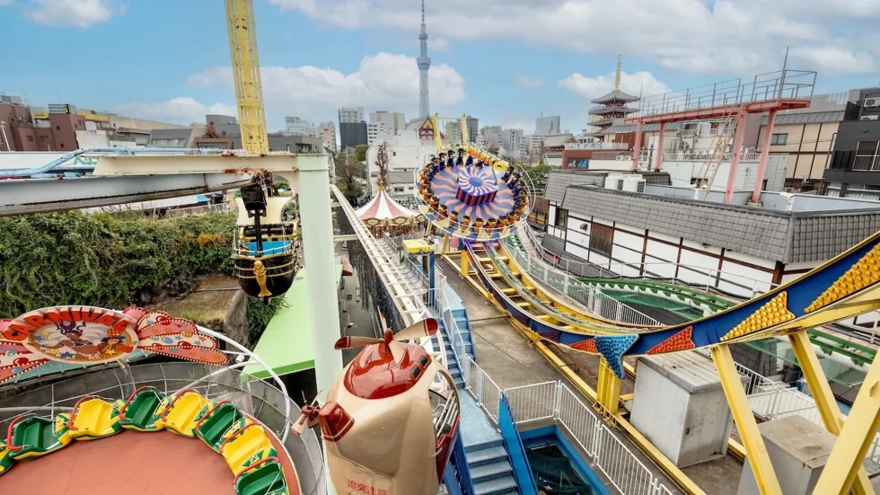 Rooftop amusement park with colorful rides and a cityscape in the background.
