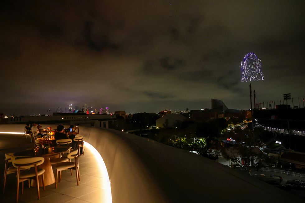 Rooftop dining with city skyline and glowing R2-D2-shaped drone display at night.