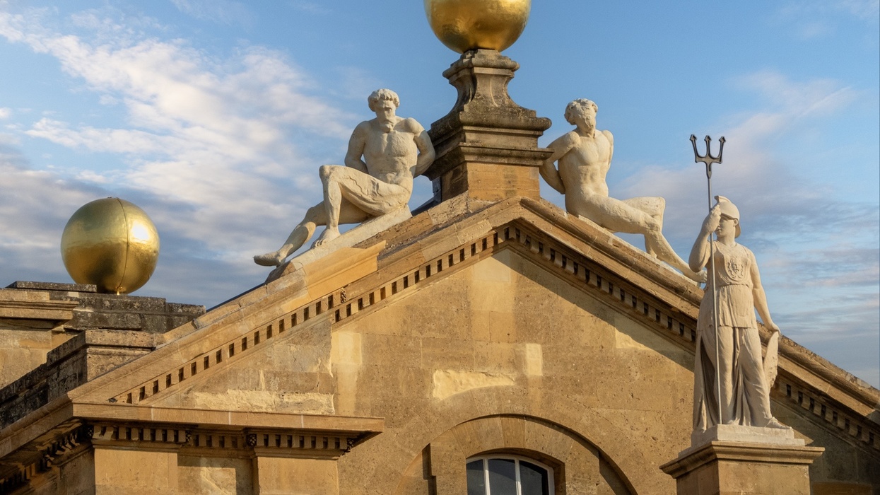 Rooftop statues and golden spheres on a historic building called Blenheim Palace under a blue sky.