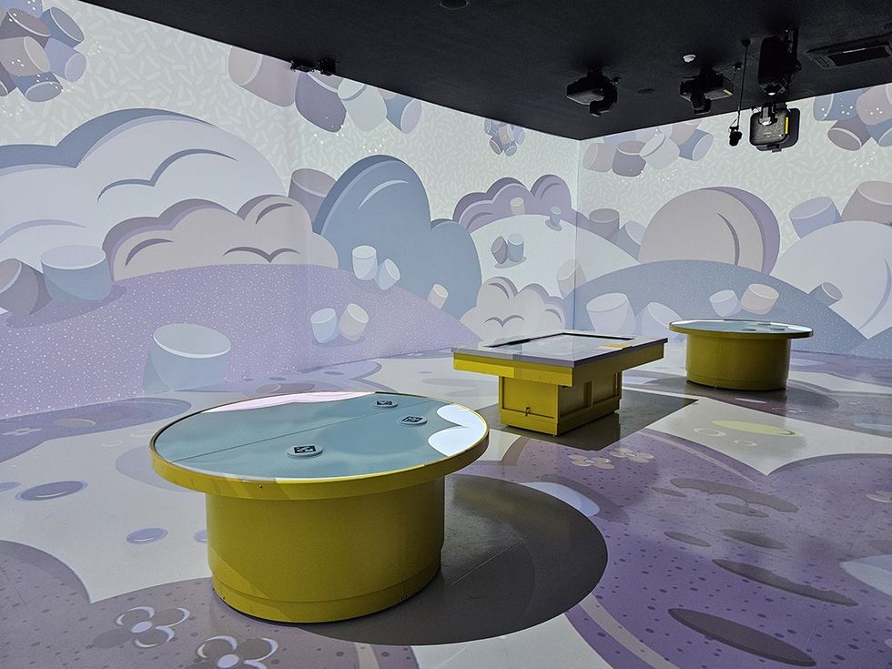 Room with round yellow tables and cartoon cloud murals on the walls.