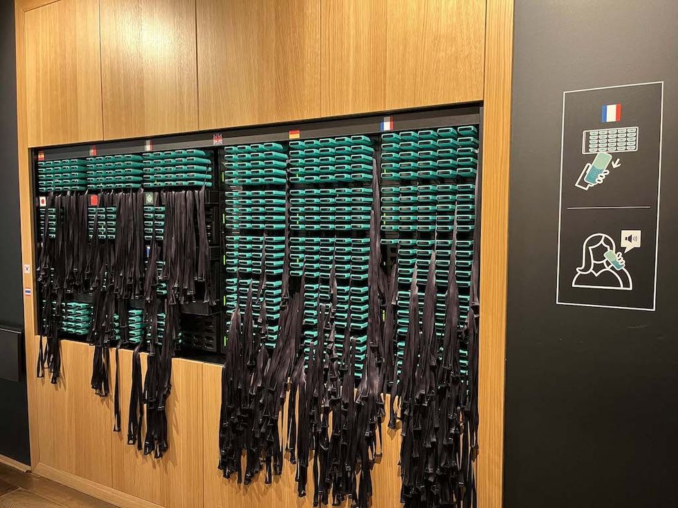 Row of black Guide-ID audio guides with teal fronts hanging on a wooden wall at Maison Cailler
