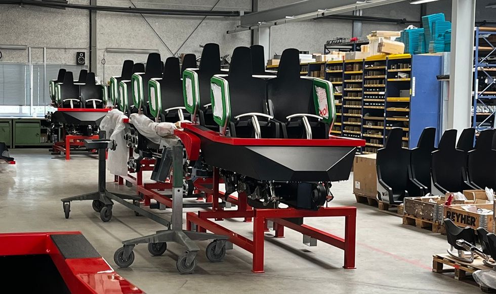 Row of black seats with green accents in a workshop setting, on red metal frames.