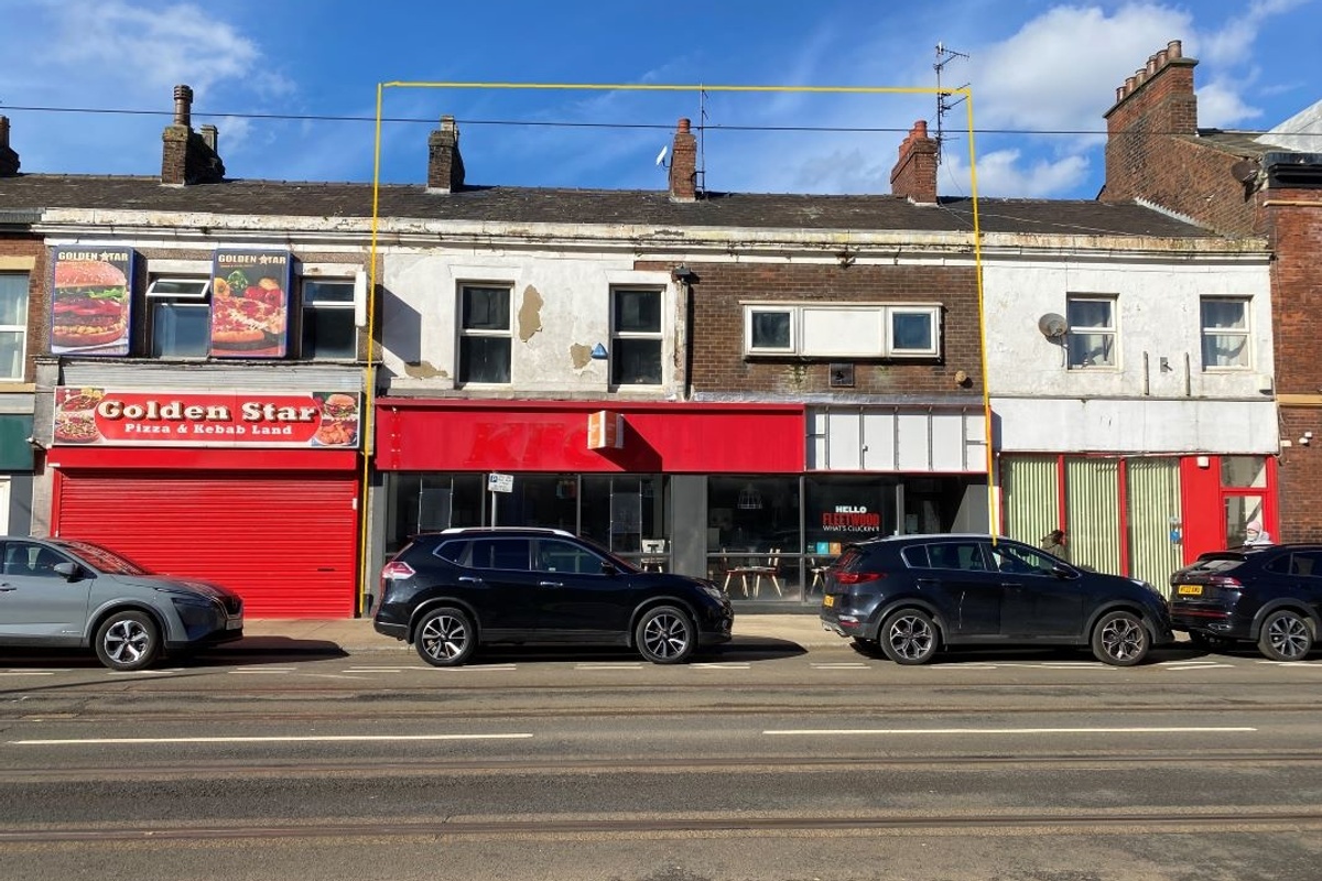 Row of shops and parked cars under a blue sky.
