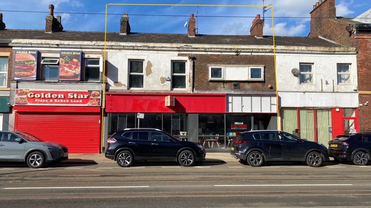 Row of shops and parked cars under a blue sky.