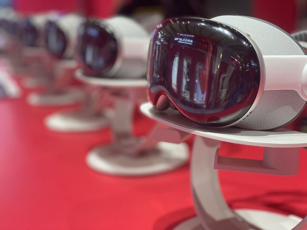 Row of VR headsets on stands with a red background.