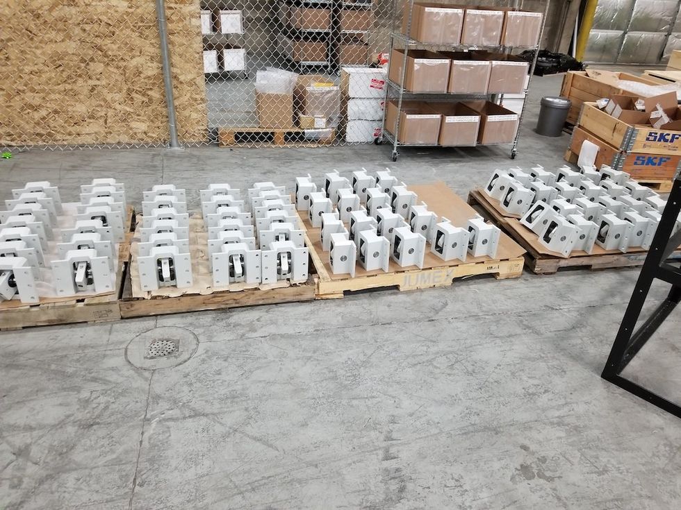 Rows of white metal brackets on wooden pallets in an industrial warehouse.
