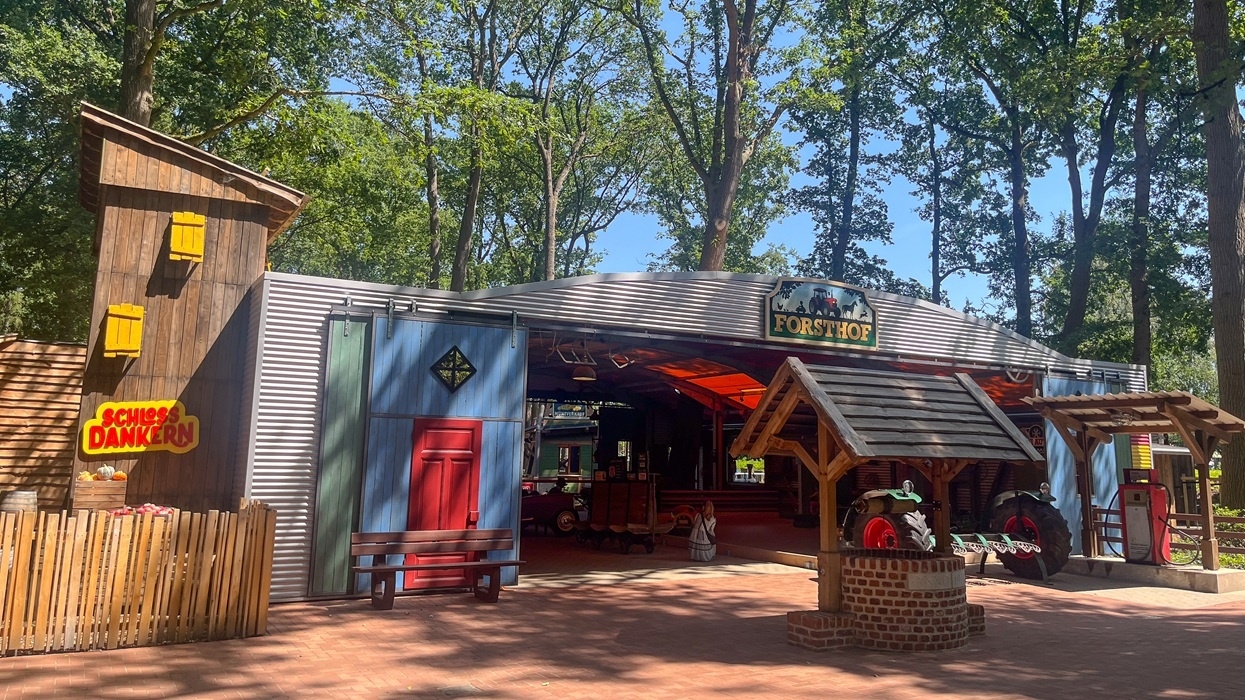 Rustic theme park building at Schloss Dankern, with tractor decor, surrounded by trees on a sunny day.