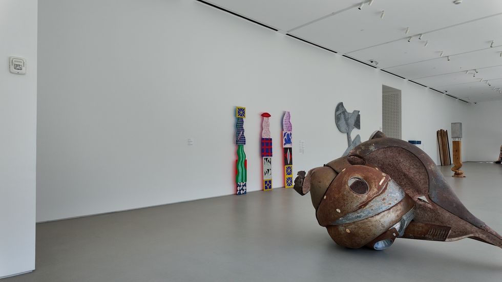 Rusty fish sculpture in modern art gallery with colorful abstract pieces on the wall.