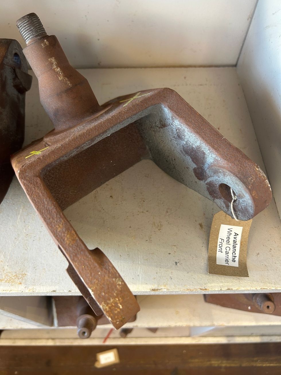 Rusty metal bracket labeled "Avalanche Wheel Carrier Front" on a white shelf.
