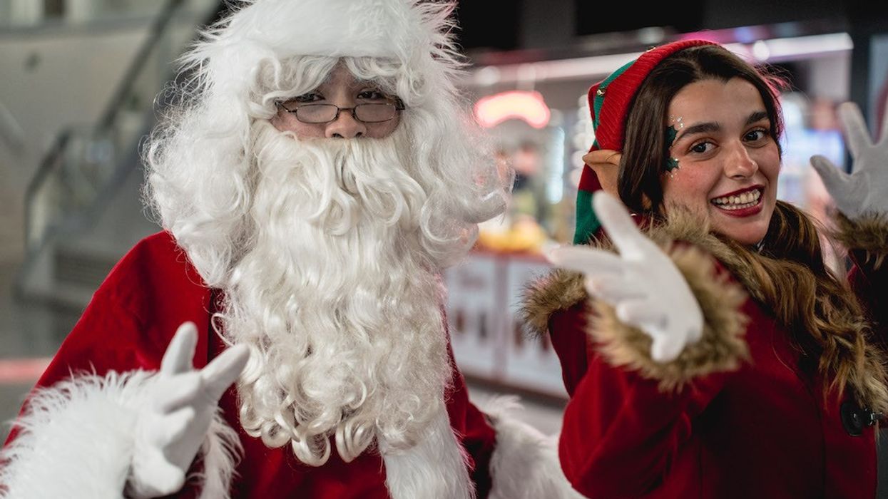 Santa and an elf smiling and posing with peace signs indoors.