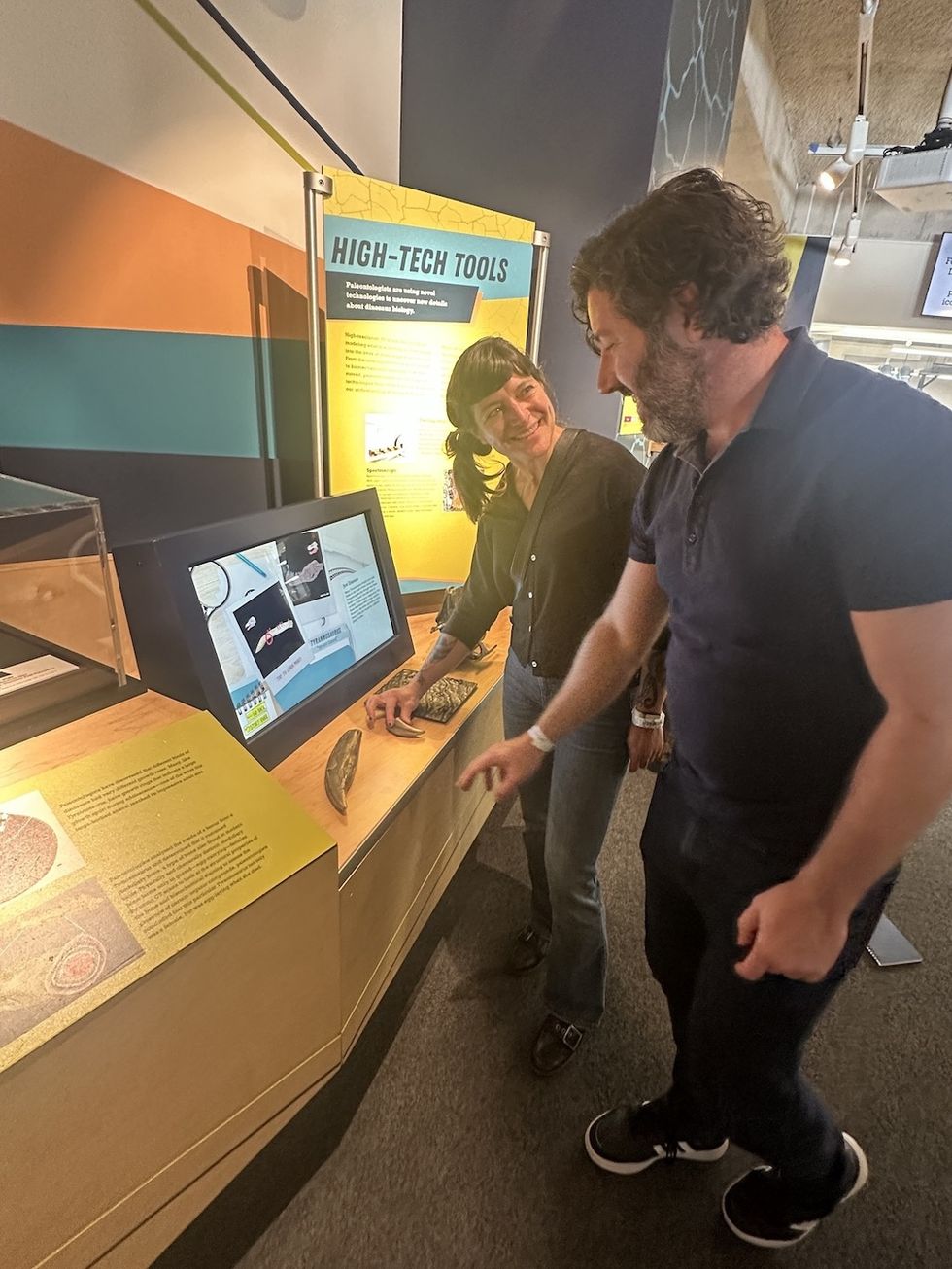 Sarah Lima and John Shaw observing dinosaur fossils at a high-tech exhibit, Frost Science