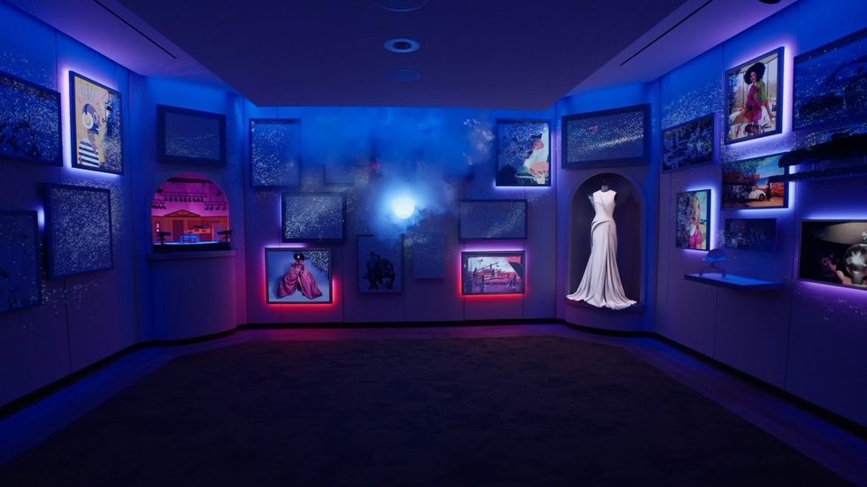 SCADstory Atlanta Dimly lit space with a white dress and colorful framed artworks on walls.
