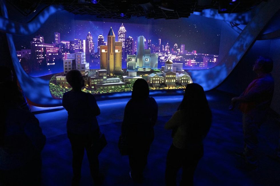 SCADstory Atlanta Silhouetted people observe a lit model cityscape in a dark, blue-lit room.