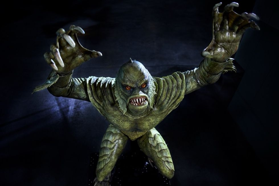Scaly creature with sharp teeth and claws reaching upwards in a dark setting.