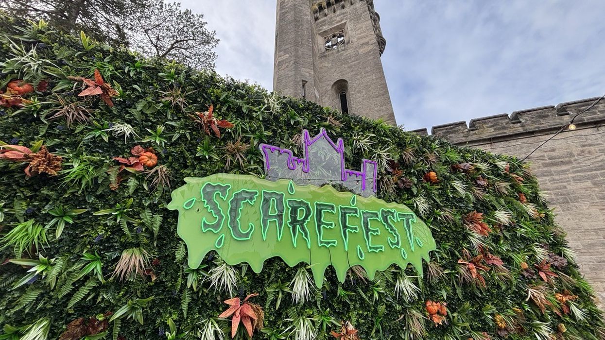 "Scarefest sign on leafy wall by castle tower under a cloudy sky."