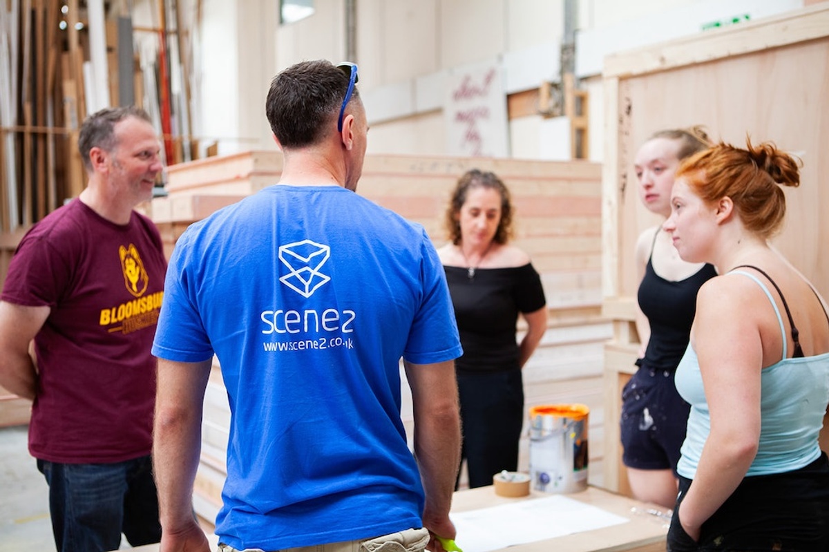Scene2 team discussing in a workshop, surrounded by wooden structures.