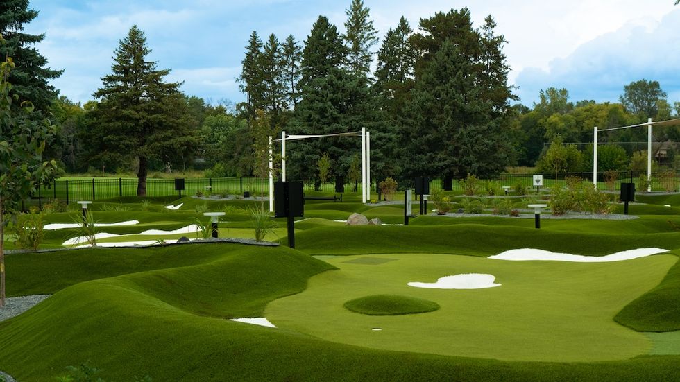 Scenic mini-golf course with lush greenery and towering trees in the background.