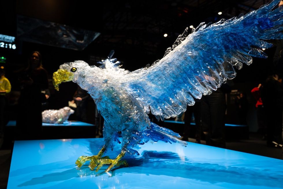 Sculpture of an eagle made from blue and clear plastic bottles on a lit display.