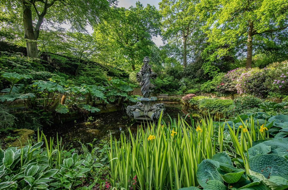 Serene garden with pond, statue, vibrant plants, and lush trees at Chester Zoo