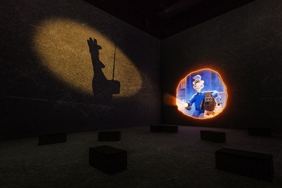 Shadow of a chef and projected animation on a dark gallery wall with seating blocks.