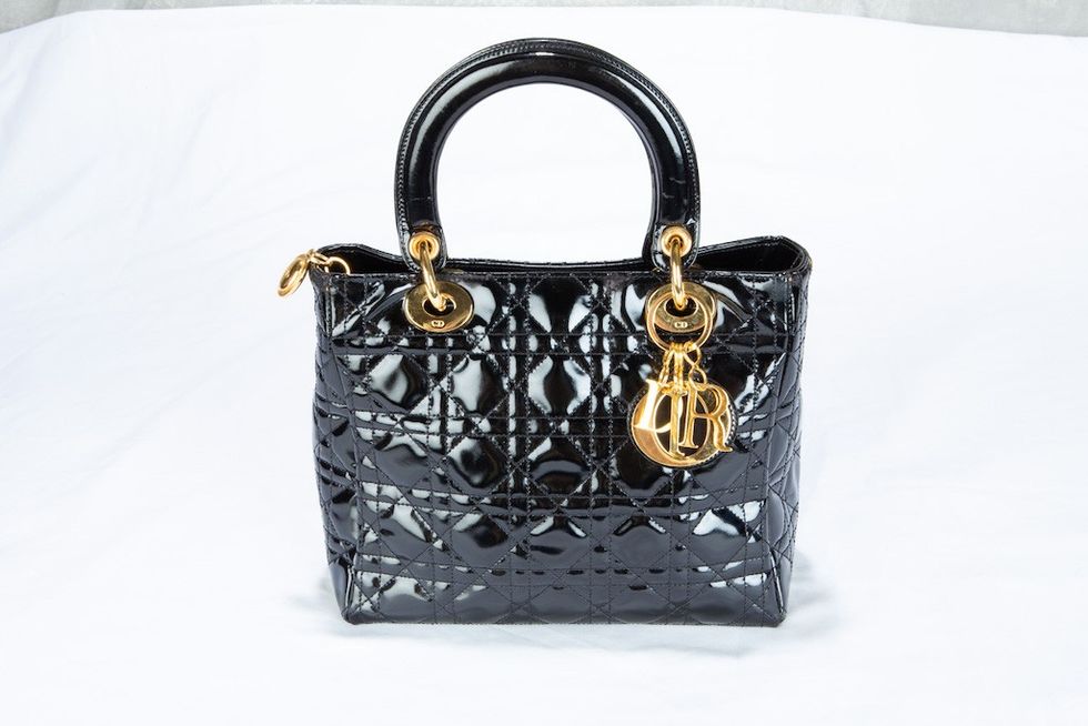 Shiny black handbag with quilted pattern and gold accents on a white background.