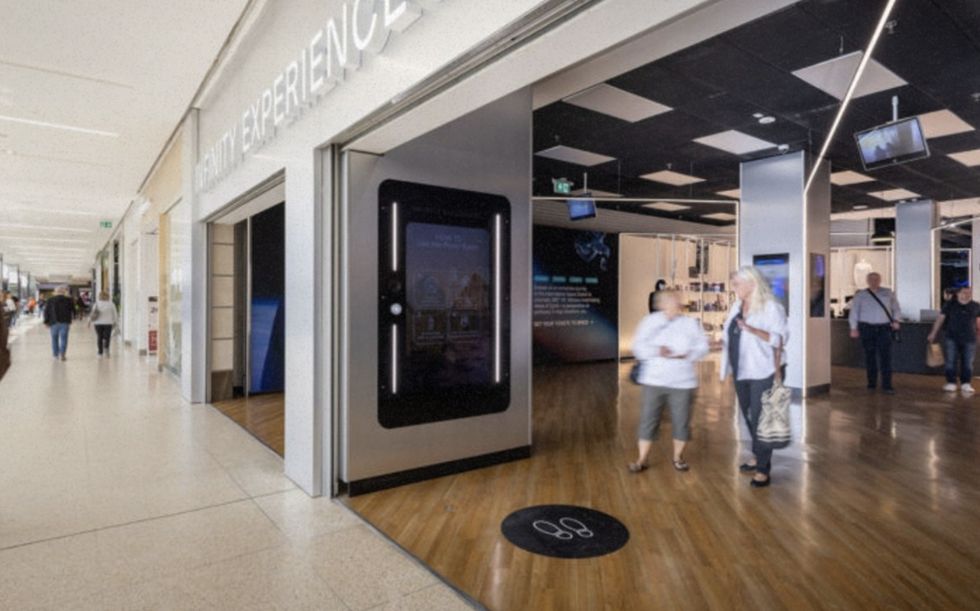 Shop entrance in a mall with digital displays and people walking nearby.