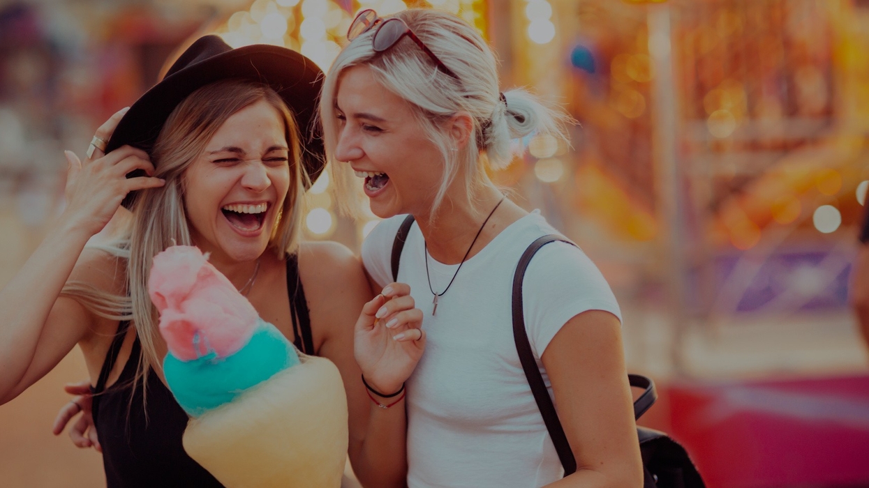 Shot of happy female friends in amusement park eating cotton candy. Two young women enjoying a day at amusement park.