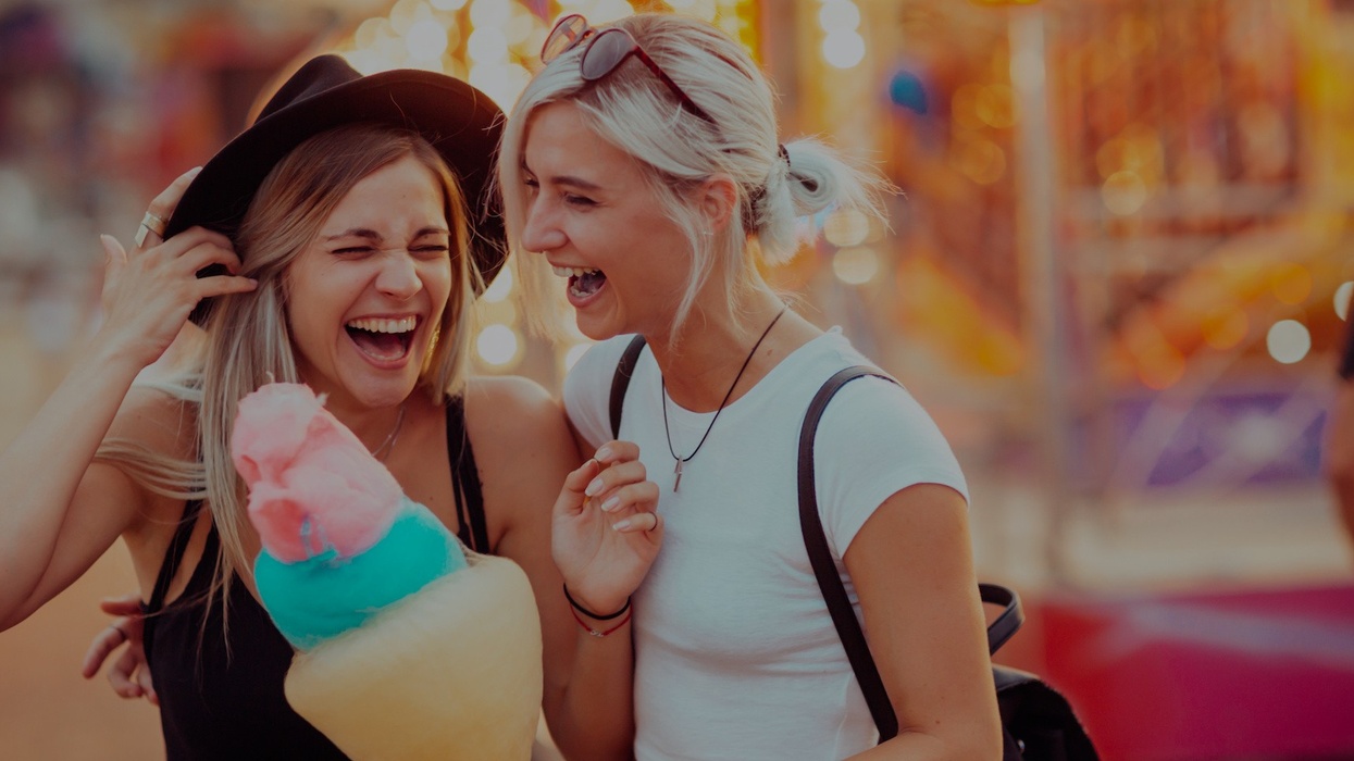 Shot of happy female friends in amusement park eating cotton candy. Two young women enjoying a day at amusement park.