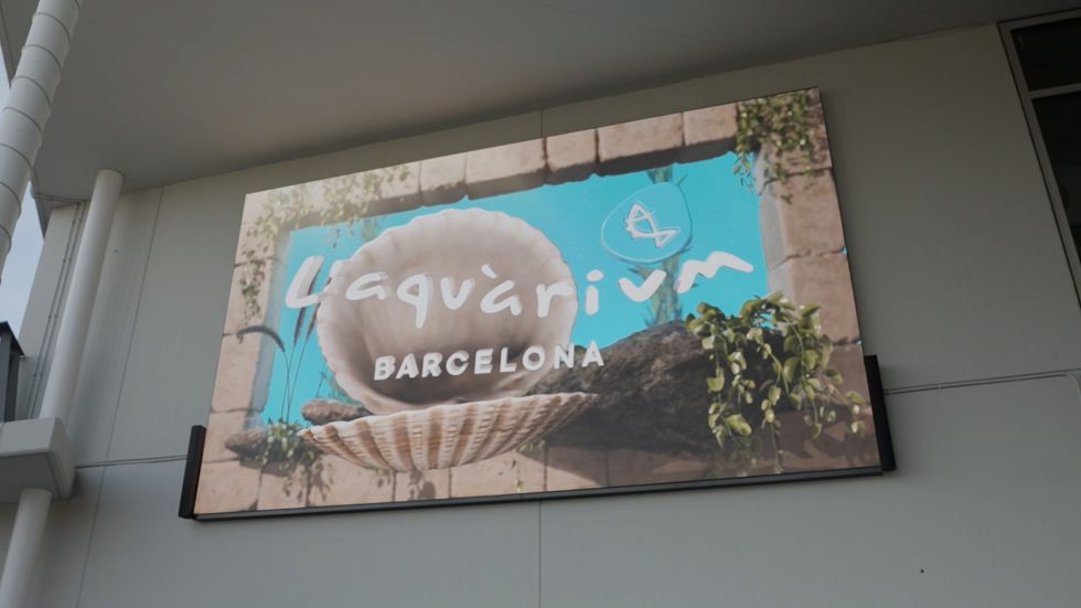 Sign for L'Aqu\u00e0rium Barcelona featuring an open seashell and plants.