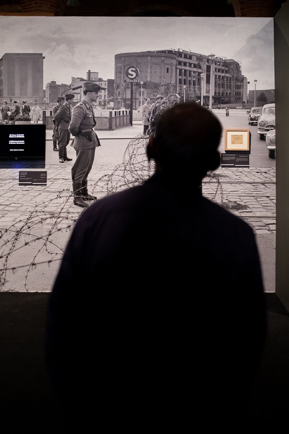 Silhouette observing a historical Berlin Wall exhibit with soldiers and barbed wire.