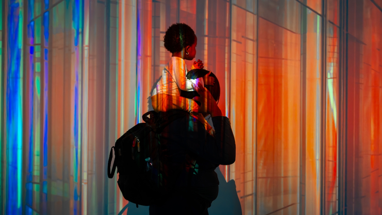 Silhouette of a parent with child against a colorful, abstract light background.