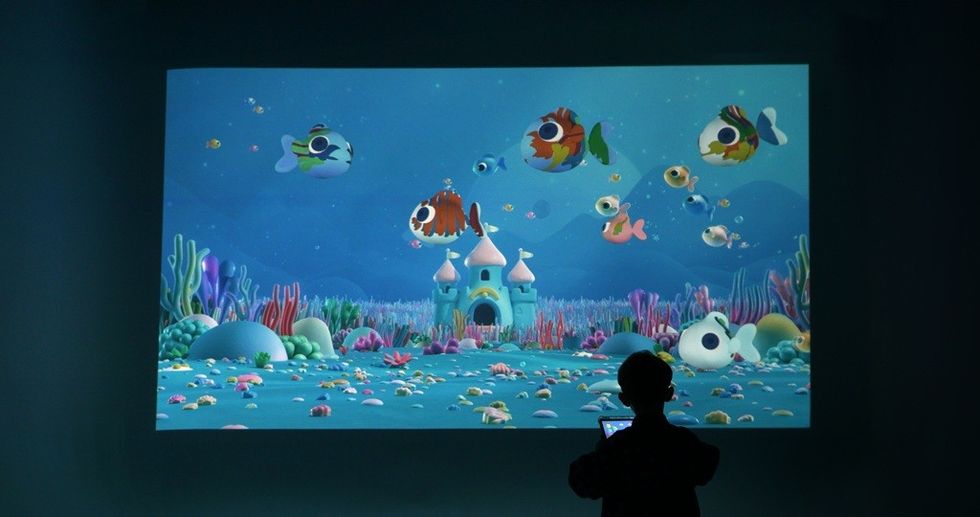 Silhouette of a person viewing an animated underwater scene on a large screen.