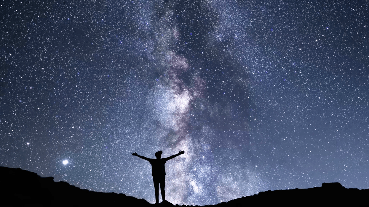 Silhouette of person against a starry night sky with the Milky Way visible.